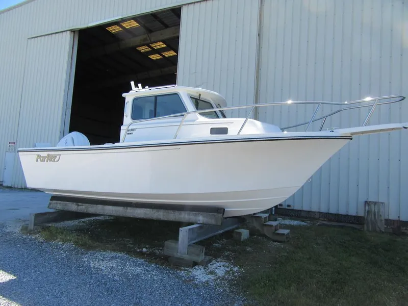 The Image of 2025 Parker 2120 Sport Cabin boat displayed outside a large warehouse. - 1