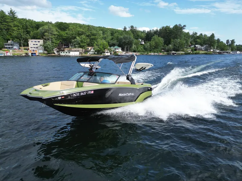 The Image of 2023 MasterCraft NXT 22 boat cruising on a lake with scenic shoreline. - 1