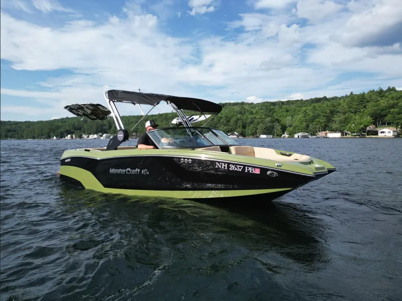 Slide: The Image of 2023 MasterCraft NXT 22 boat cruising on a lake with scenic forest background. - 30