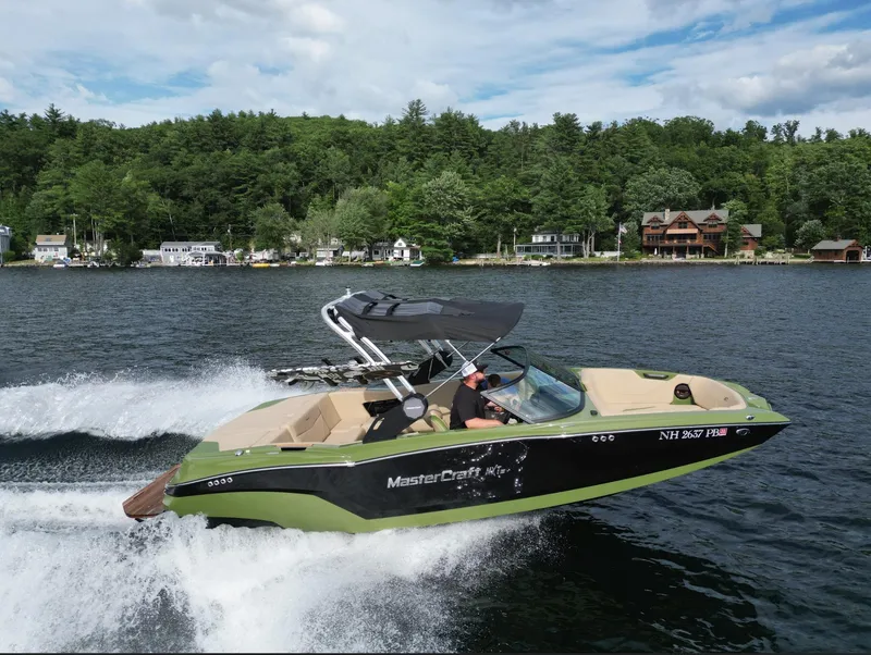 Slide: The Image of 2023 MasterCraft NXT 22 speedboat cruising on a lake with lush green shoreline. - 35