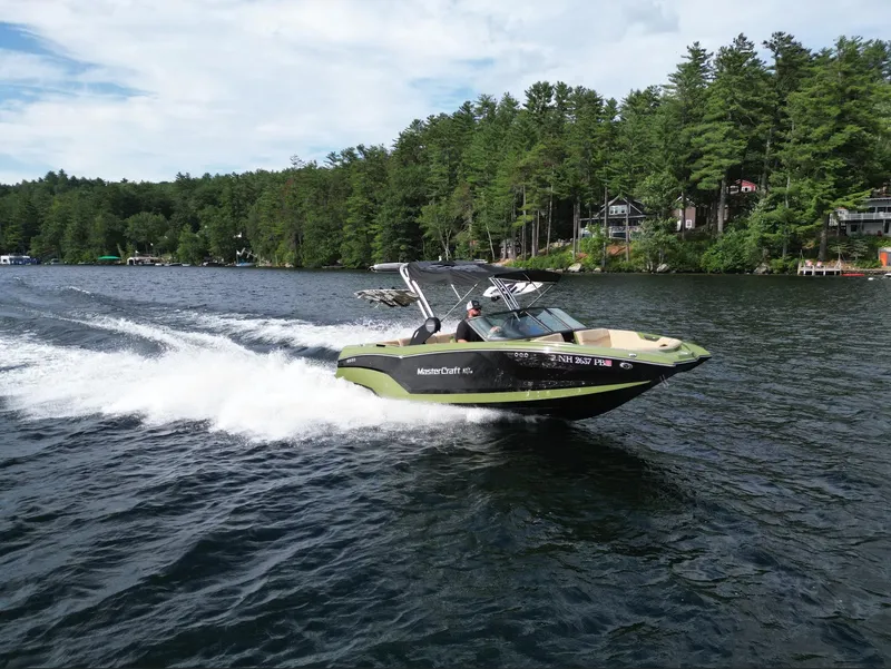 Slide: The Image of 2023 MasterCraft NXT 22 boat cruising on a lake surrounded by trees. - 37