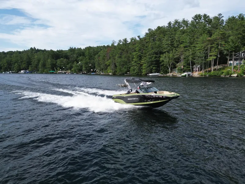 Slide: The Image of 2023 MasterCraft NXT 22 boat cruising on a lake with forested shoreline. - 39