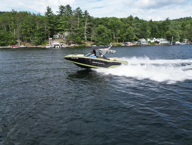 Slide: The Image of 2023 MasterCraft NXT 22 speedboat cruising on a lake with forested shoreline. - 41