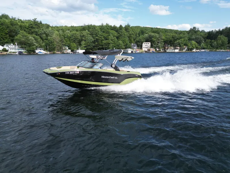 Slide: The Image of 2023 MasterCraft NXT 22 speedboat cruising on a lake with forested shoreline. - 42