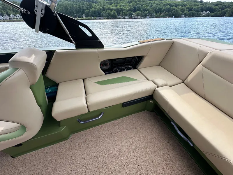 Slide: The Image of 2023 MasterCraft NXT 22 boat interior with beige and green seating by a lake. - 8