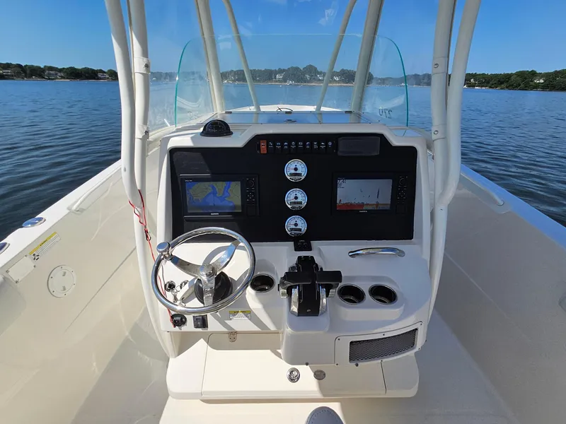 Slide: The Image of 2016 Sailfish 270 CC boat dashboard with navigation screens and steering wheel on calm water. - 15