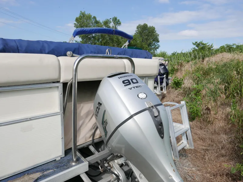 Slide: The Image of 2005 Odyssey Pontoons Millenium 2 with Honda 90 outboard motor, docked near grassy shore. - 2