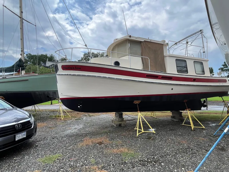 Slide: The Image of 1998 Nordic Tug 32 boat on stands, with overcast sky and nearby vehicles. - 39