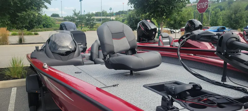 Slide: The Image of 2024 Tracker Pro Team 190 TX boat, red and gray, parked outdoors with lush greenery. - 2