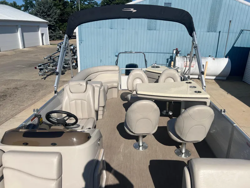 Slide: The Image of 2017 Bennington 24SPDX pontoon boat with seating and table, docked near blue building. - 12