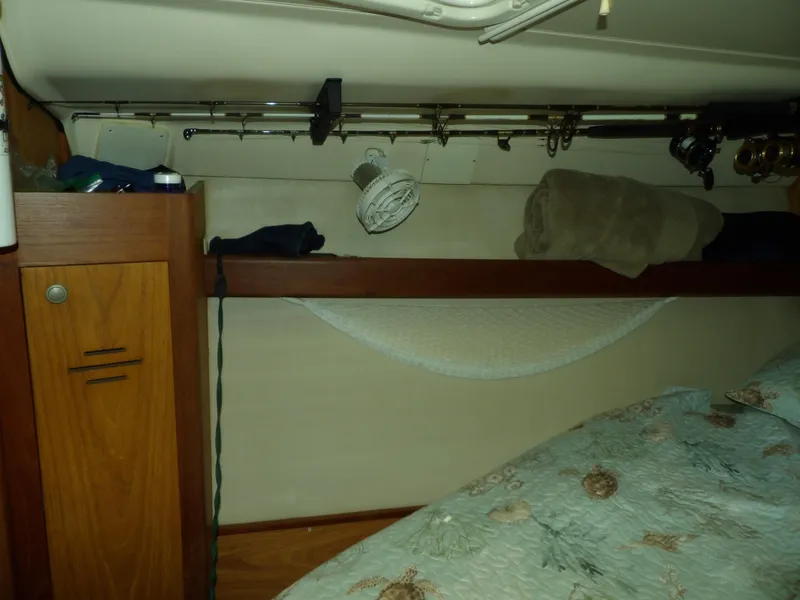 Slide: The Image of 2000 Hunter 460 boat interior with storage shelf, fishing rods, and bedding. - 44