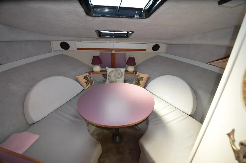 Slide: The Image of 1988 Carver 27 Montego cabin interior with round table, cushioned seating, and decorative pillows. - 18