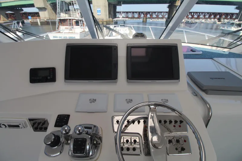 Slide: The Image of Helm of 2013 Cabo 40 Hardtop Express with dual screens and controls, docked near a bridge. - 27