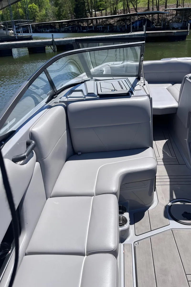 Slide: The Image of 2024 Moomba Max boat interior with gray seating and open deck, docked by the water. - 17
