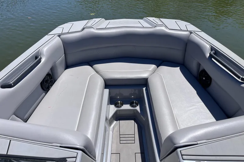 Slide: The Image of 2024 Moomba Max boat interior with gray seating and cup holders on a calm lake. - 6