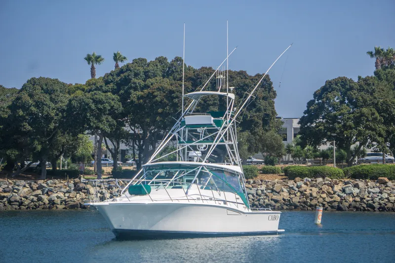 Slide: The Image of 1997 Cabo 35 Express boat on calm water near rocky shoreline and trees. - 2