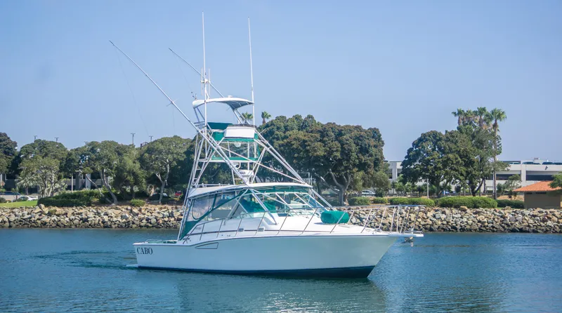 Slide: The Image of 1997 Cabo 35 Express boat cruising on calm water near a rocky shoreline. - 3
