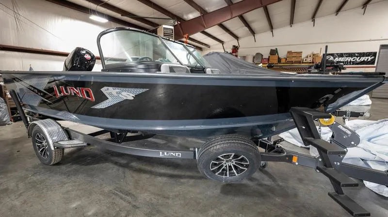 The Image of 2024 Lund 1875 Crossover XS boat in a warehouse, on a trailer, side view. - 1