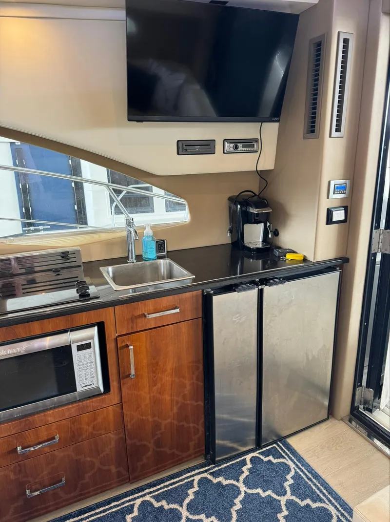 Slide: The Image of 2015 Carver C37 Coupe kitchen area with sink, microwave, fridge, and TV. - 22