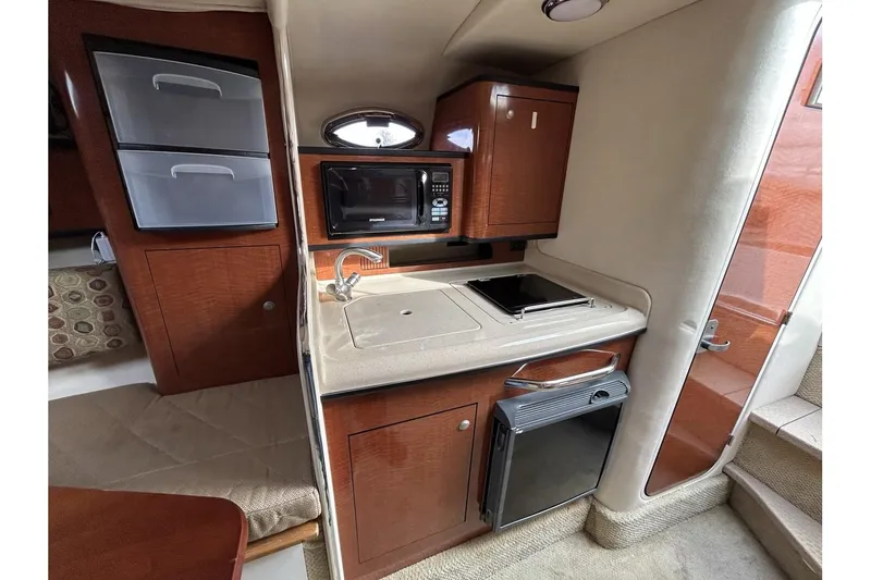 Slide: The Image of 2005 Sea Ray 280 Sundancer interior kitchen with microwave, sink, and storage cabinets. - 14