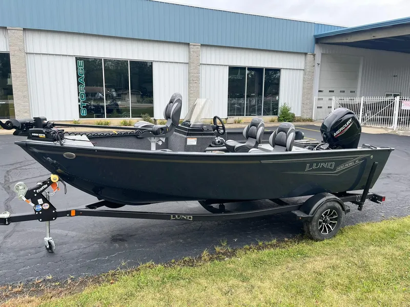 Slide: The Image of 2025 Lund 1650 Rebel XL SS fishing boat on trailer, parked outside a building. - 2