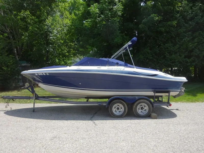 Slide: The Image of 2006 Four Winns H220 boat on trailer, parked on a road with lush green trees. - 21