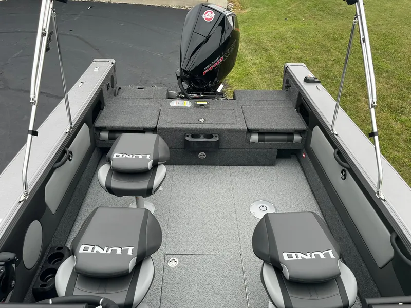 Slide: The Image of 2025 Lund 1875 Tyee boat interior with seating and motor, parked on grass. - 8