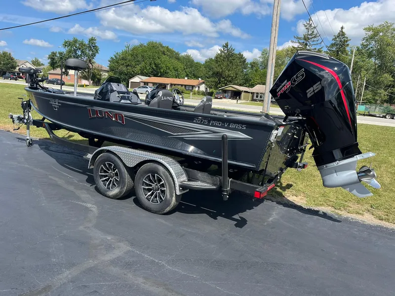 Slide: The Image of 2025 Lund 2075 Pro-V Bass XS boat on trailer, parked outdoors under blue sky. - 4