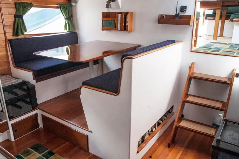 Slide: The Image of Interior of a 1996 Custom Bolger PH Shoal-draft Ketch with wooden dining area and steps. - 4