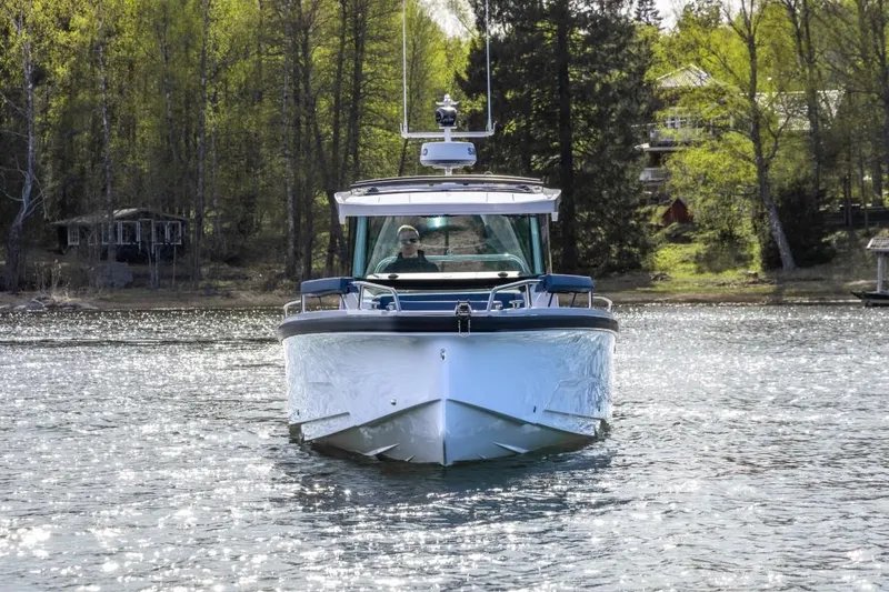 Slide: The Image of 2025 Axopar 29 XC Cross Cabin boat on a serene lake with forest backdrop. - 2