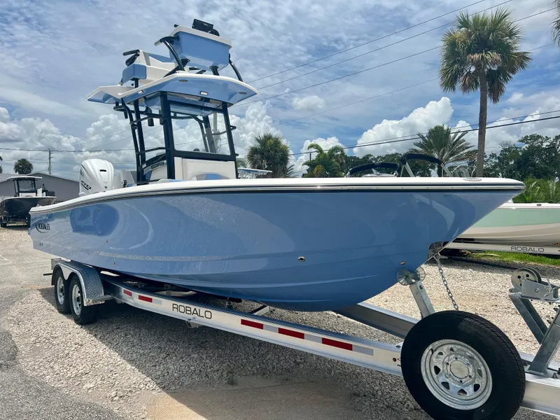 Slide: The Image of 2025 Robalo 266 Cayman SD boat on trailer, blue hull, palm trees in background. - 2