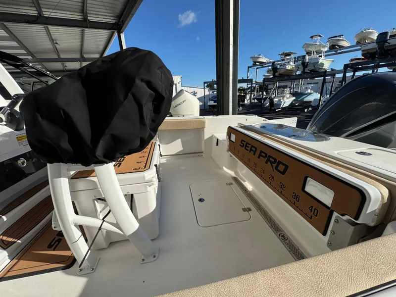 Slide: The Image of 2025 Sea Pro 242 Center Console boat interior, featuring seating and storage under a covered dock. - 6