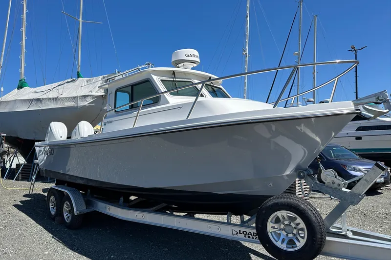 Slide: The Image of 2025 Parker 2420 Sport Cabin boat on trailer, parked outdoors under clear blue sky. - 14