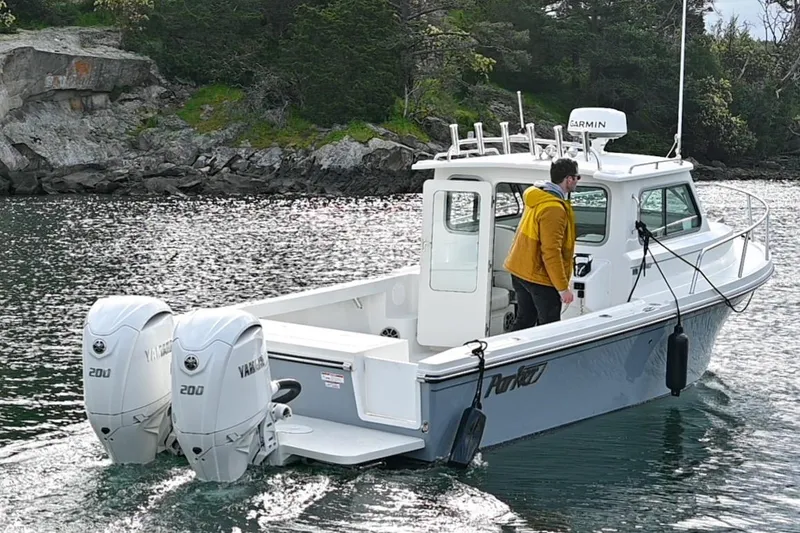 Slide: The Image of 2025 Parker 2420 Sport Cabin boat cruising on a scenic lake with lush greenery. - 3