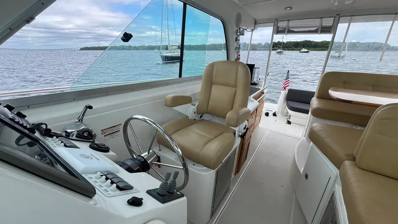 Slide: The Image of 2014 Back Cove 34 boat interior with helm, beige seating, and scenic water view. - 19