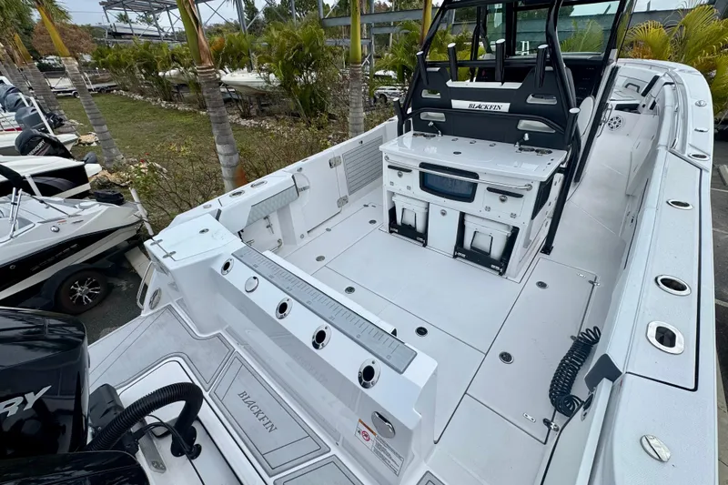 Slide: The Image of 2025 Blackfin 332 CC boat interior with fishing rod holders and seating, docked near palm trees. - 69