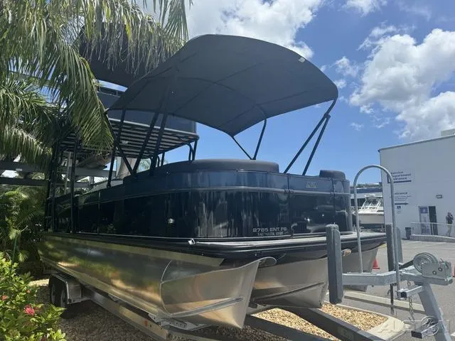 Slide: The Image of 2024 Avalon Catalina Entertainer Funship 27 FT pontoon boat on trailer under palm trees. - 7