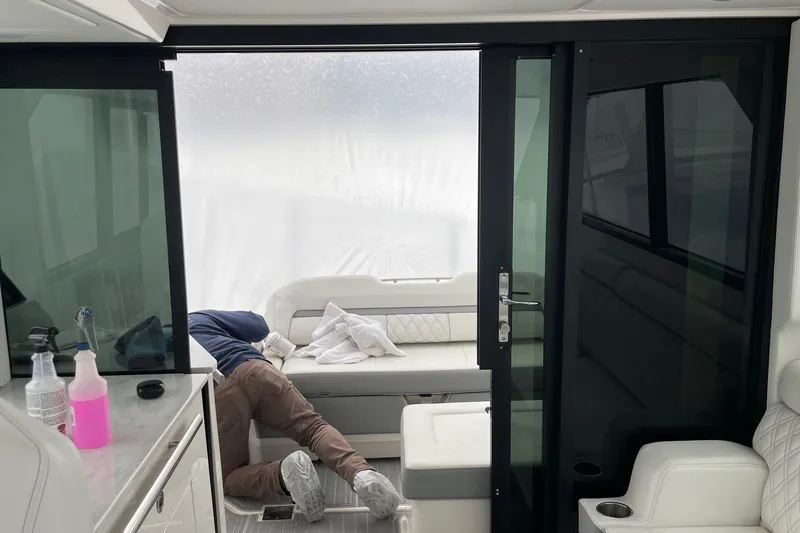 Slide: The Image of Interior of 2025 Regal 36 Grande Coupe with person cleaning, featuring modern seating and glass doors. - 61