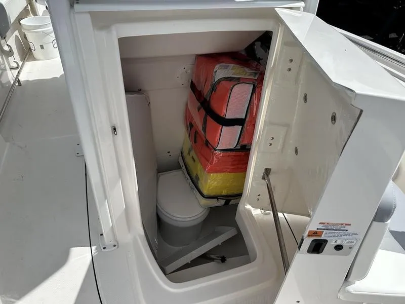 Slide: The Image of 2022 Robalo R242 boat storage compartment with life jackets and a portable toilet. - 18