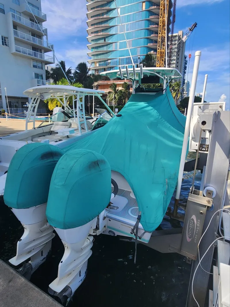 Slide: The Image of 2018 Contender 24 Sport boat with teal cover docked near modern buildings. - 18