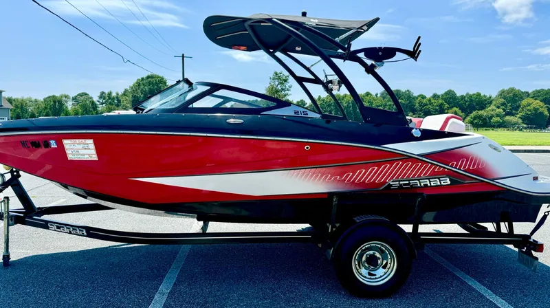 Slide: The Image of 2015 Scarab 215 HO Impulse boat, red and black, parked on trailer. - 21