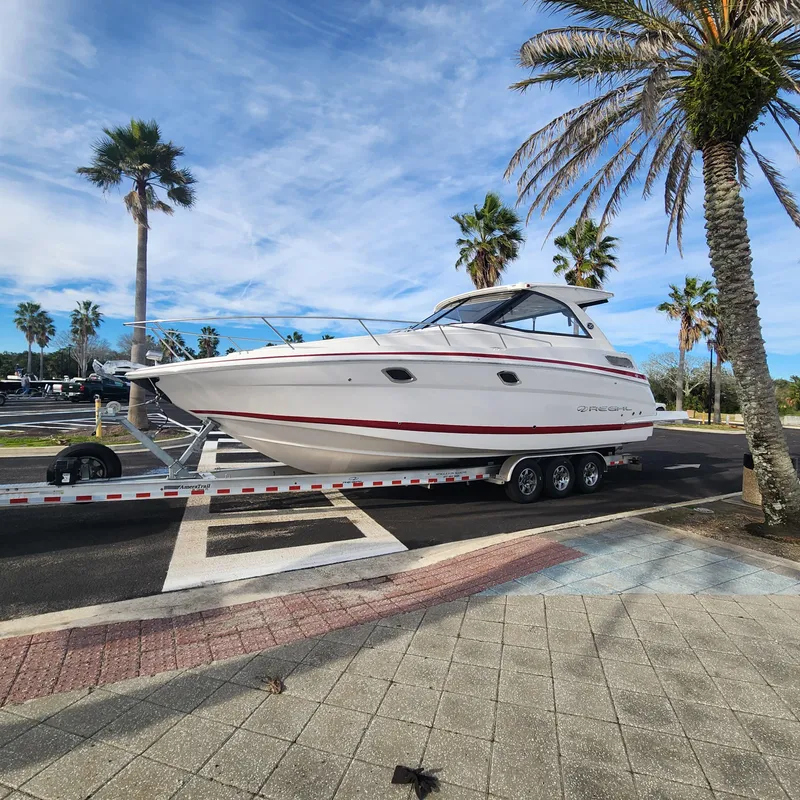 Slide: The Image of 2018 Regal 35 Sport Coupe boat on a trailer, parked near palm trees. - 4
