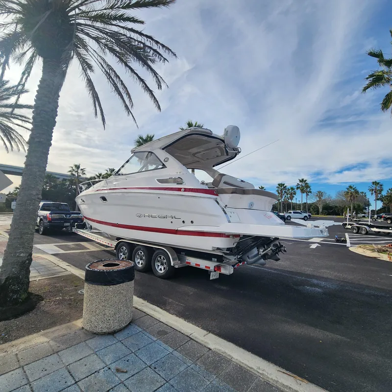 Slide: The Image of 2018 Regal 35 Sport Coupe boat on a trailer in a parking lot with palm trees. - 5