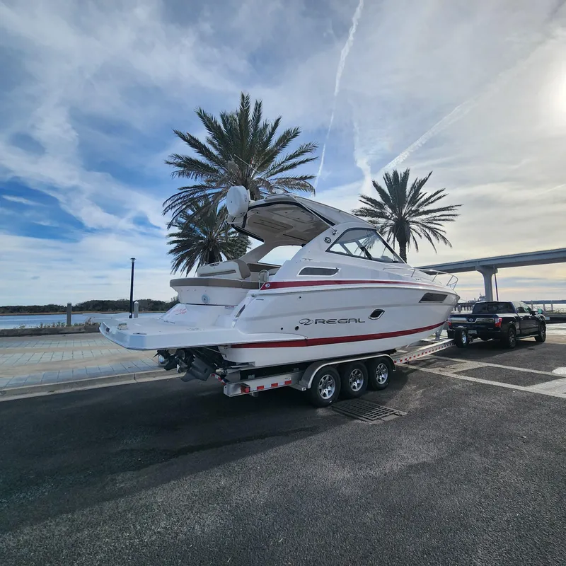Slide: The Image of 2018 Regal 35 Sport Coupe boat on a trailer, parked near palm trees and waterfront. - 6