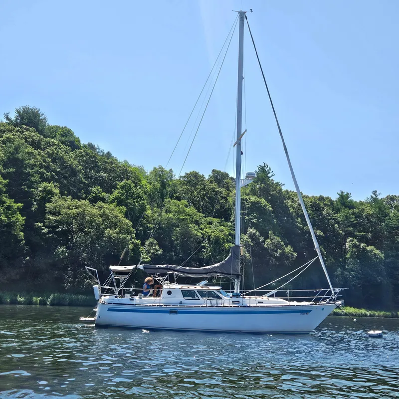 Slide: The Image of 1986 Nautilus Pilothouse 36 sailboat on a serene lake with lush green trees. - 0