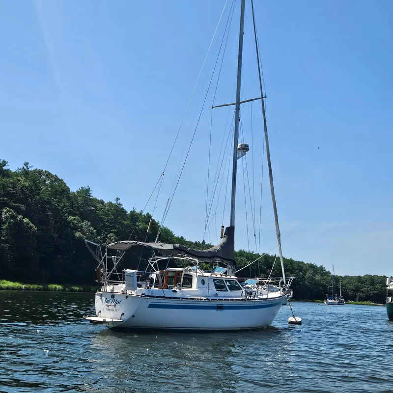 Slide: The Image of 1986 Nautilus Pilothouse 36 sailboat anchored on a calm river under clear blue skies. - 3