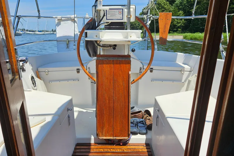 Slide: The Image of 1986 Nautilus Pilothouse 36 sailboat cockpit with wooden steering wheel and serene water view. - 36