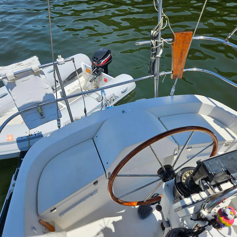 Slide: The Image of 1986 Nautilus Pilothouse 36 cockpit with steering wheel, adjacent to a small dinghy on water. - 40