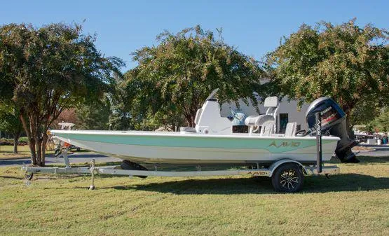 Slide: The Image of 2024 Avid 21 FSX boat on trailer, parked on grass with trees in background. - 2