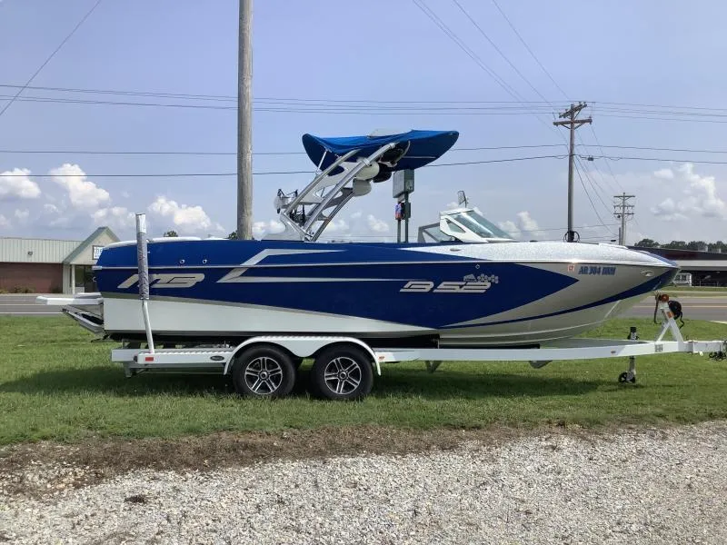 Slide: The Image of 2016 MB B52 23 boat on a trailer, blue and white, parked on grass. - 1